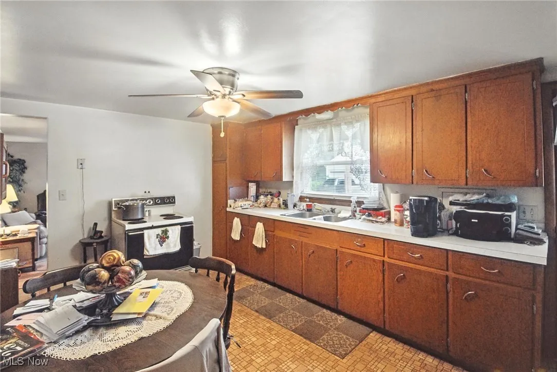 Kitchen with light countertops, electric stove, ceiling fan, brown cabinetry, and tile patterned floors