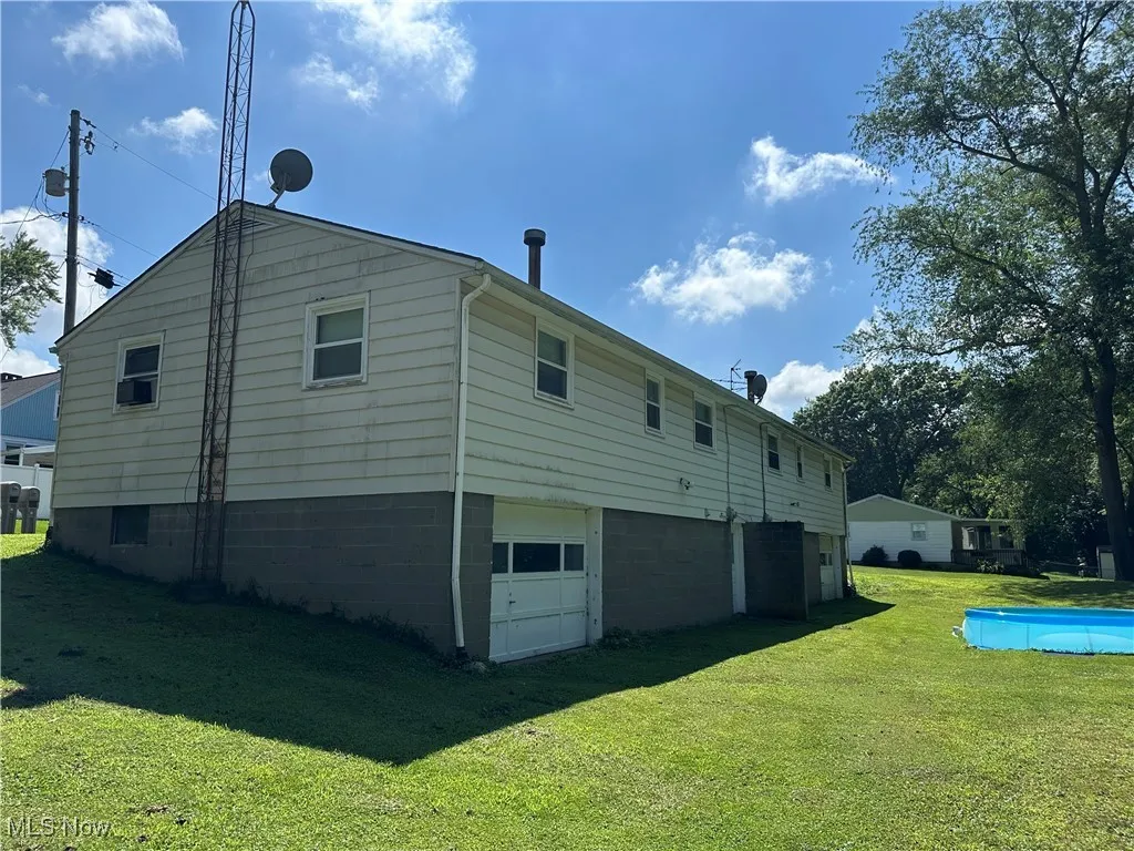 Rear view of property featuring an attached garage, a yard, and an outdoor pool
