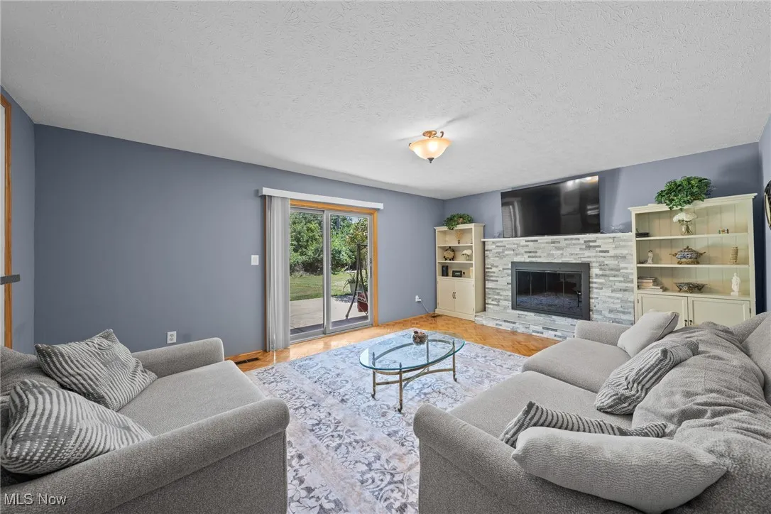 Living area with a textured ceiling, wood finished floors, and a glass covered fireplace