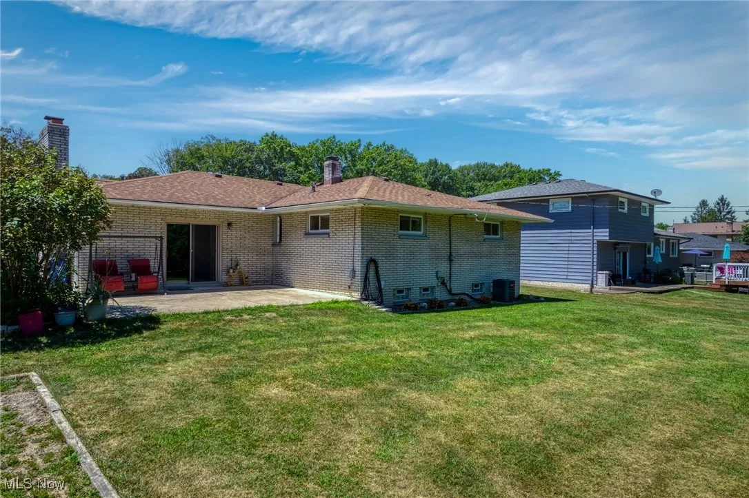 Back of property featuring a patio, brick siding, a lawn, a chimney, and a shingled roof