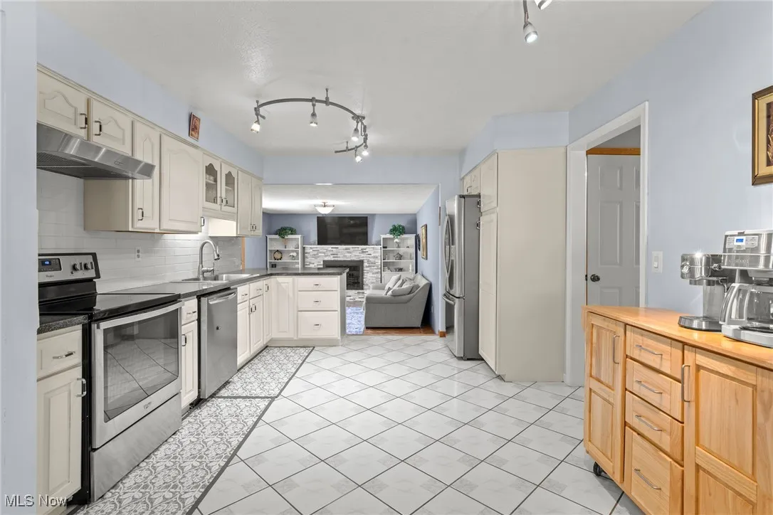 Kitchen featuring appliances with stainless steel finishes, tasteful backsplash, under cabinet range hood, a peninsula, and light tile patterned floors