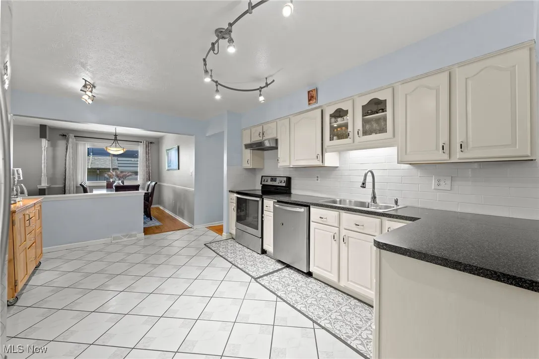 Kitchen featuring appliances with stainless steel finishes, dark countertops, decorative backsplash, under cabinet range hood, and light tile patterned flooring