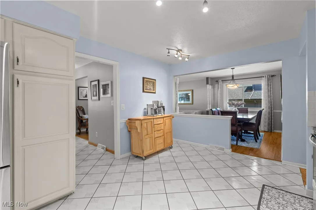 Kitchen featuring light tile patterned floors, freestanding refrigerator, white cabinets, and decorative light fixtures