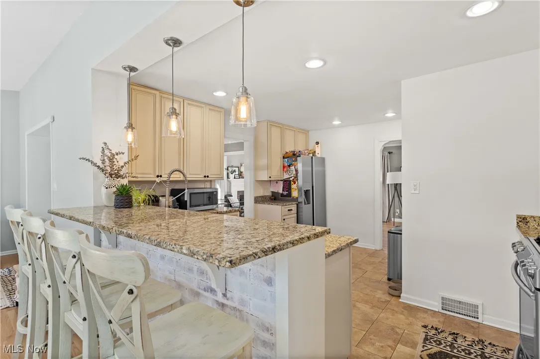 Kitchen with cream cabinetry, a peninsula, a kitchen bar, appliances with stainless steel finishes, and recessed lighting
