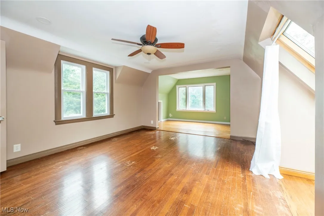 Primary Bedroom with hardwood flooring, vaulted ceiling, a skylight that opens up and ceiling fan