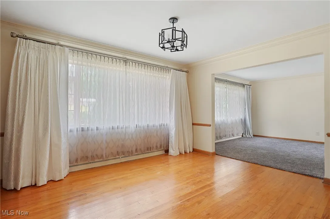Empty room with wood finished floors, crown molding, a baseboard heating unit, and a chandelier