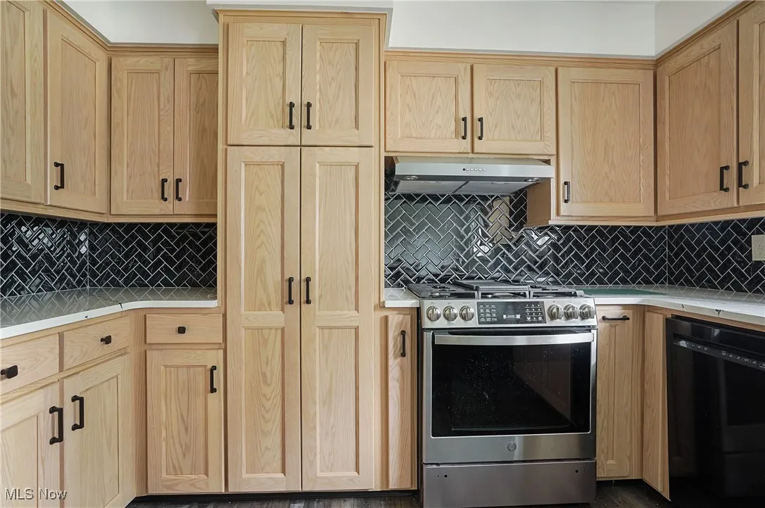 Kitchen with light brown cabinets, stainless steel range with gas stovetop, light countertops, dishwasher, and exhaust hood