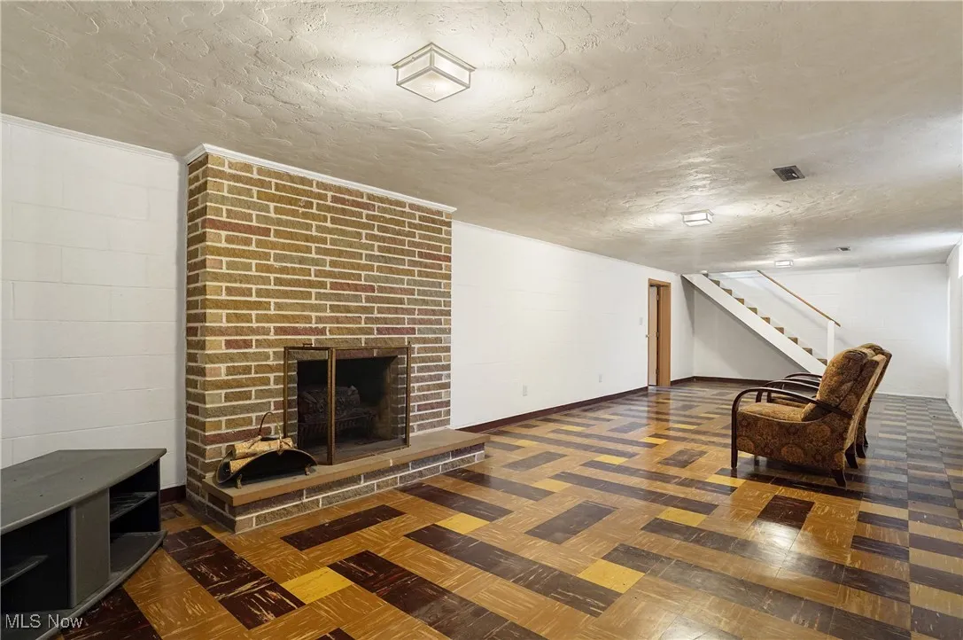 Unfurnished room with a textured ceiling, stairway, and a brick fireplace