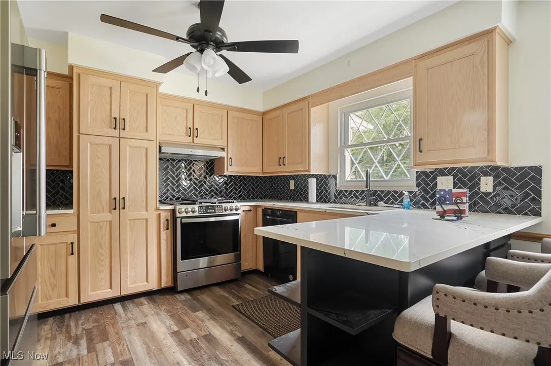 Kitchen featuring light brown cabinetry, a peninsula, appliances with stainless steel finishes, dark wood finished floors, and ceiling fan