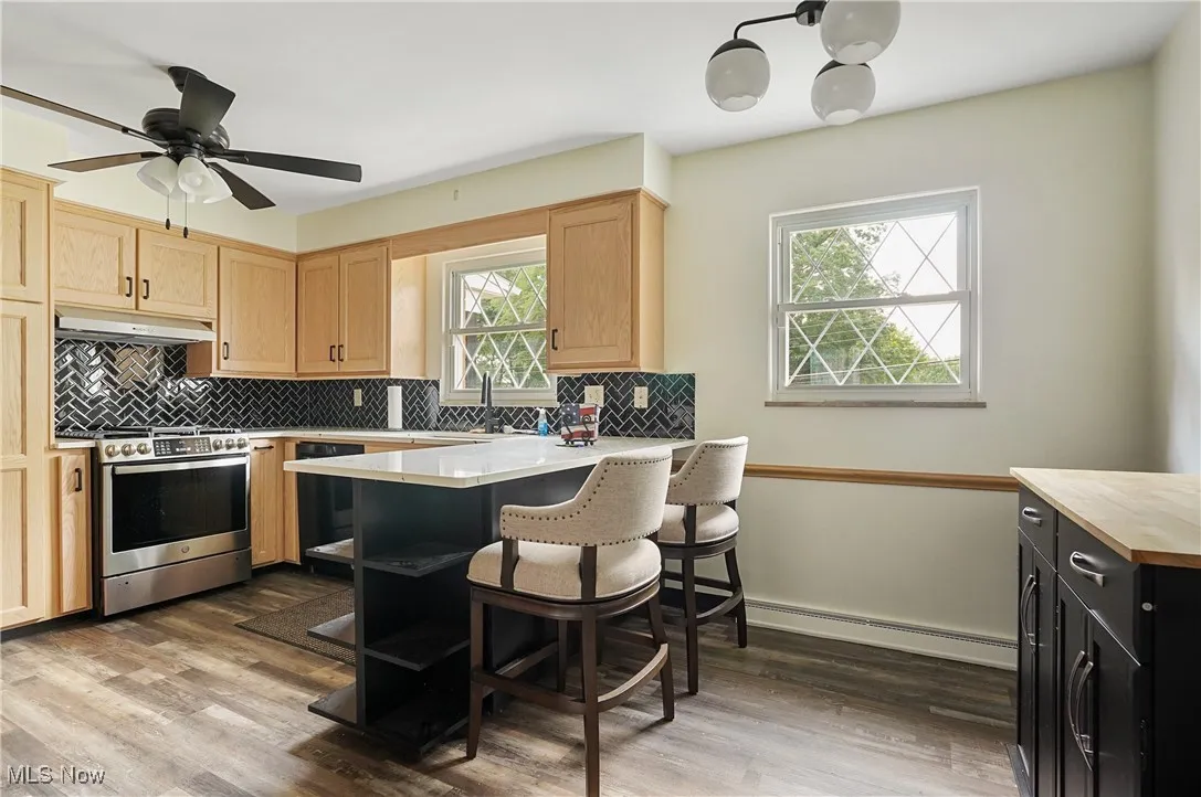 Kitchen with light countertops, light brown cabinets, gas stove, tasteful backsplash, and wood finished floors