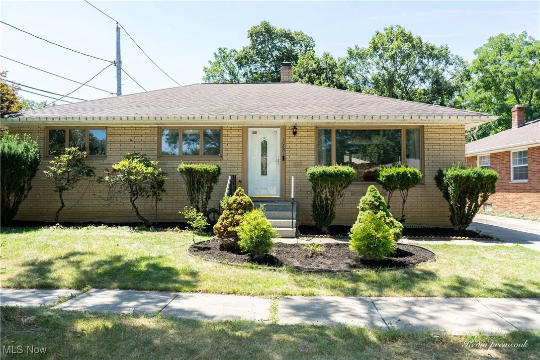 Ranch-style home with a chimney, brick siding, a shingled roof, and a front yard