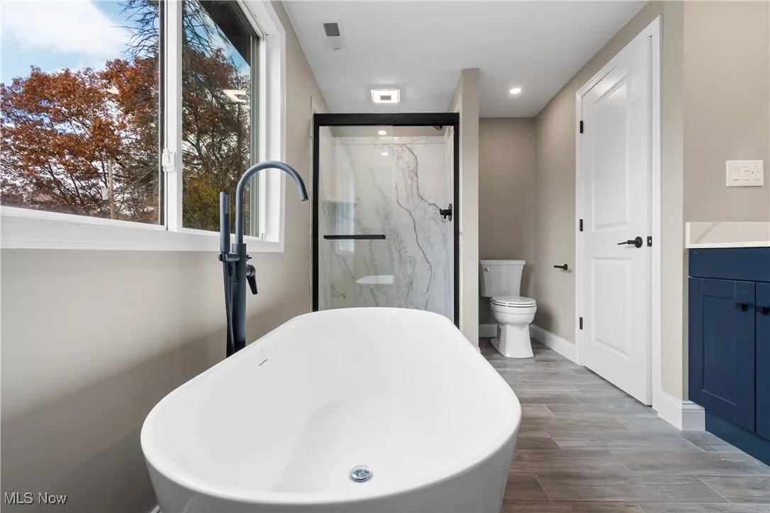 Full bathroom with wood finished floors, a freestanding tub, a marble finish shower, recessed lighting, and vanity