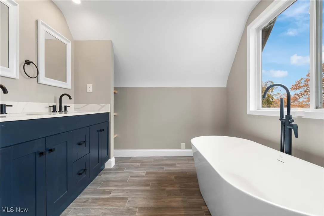 Bathroom featuring lofted ceiling, double vanity, wood finished floors, and a freestanding bath