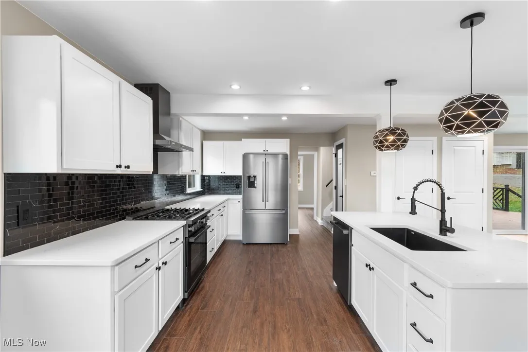Kitchen with appliances with stainless steel finishes, decorative backsplash, dark wood-type flooring, wall chimney range hood, and white cabinetry
