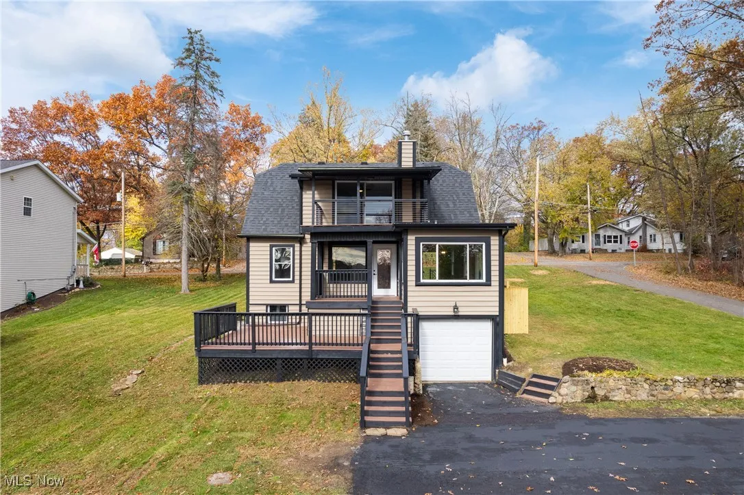 View of front of home with a balcony, a chimney, roof with shingles, a garage, and asphalt driveway