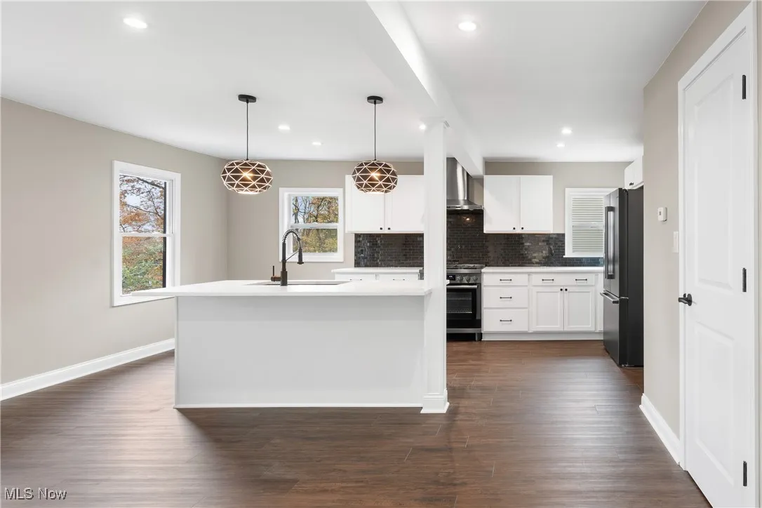 Kitchen with dark wood-style floors, high end refrigerator, range with gas stovetop, white cabinetry, and wall chimney exhaust hood