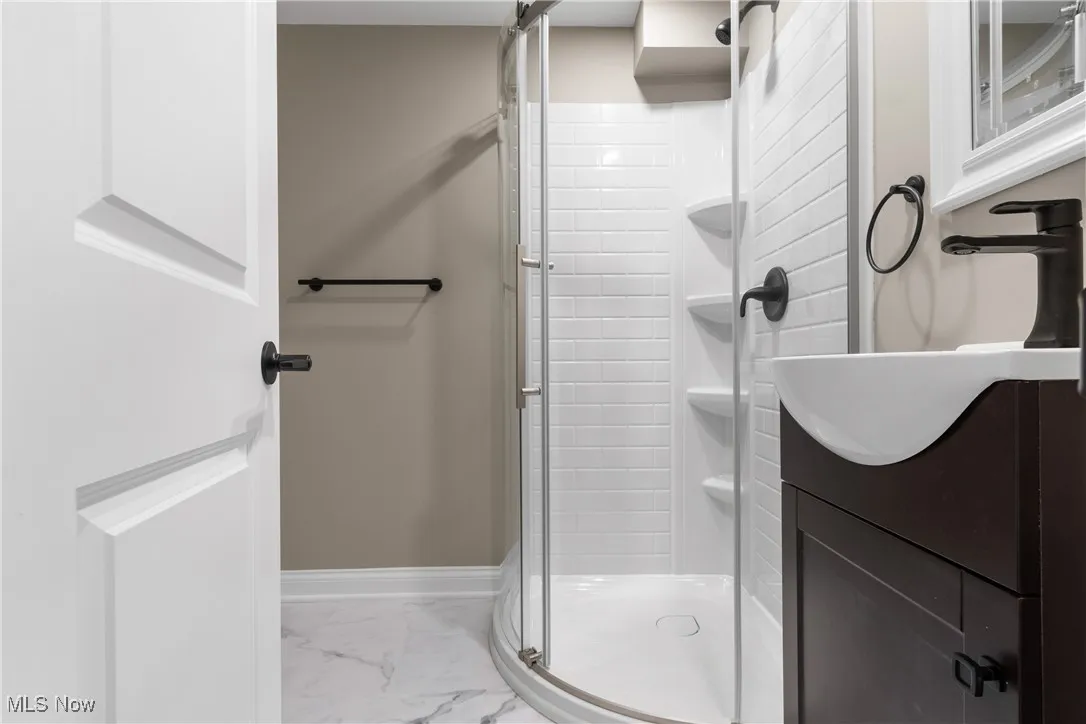 Full bath with a shower stall, marble look tile flooring, and vanity