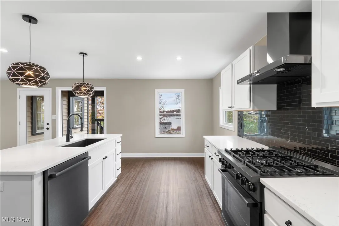 Kitchen with black gas range, recessed lighting, dark wood-style flooring, wall chimney range hood, and dishwasher