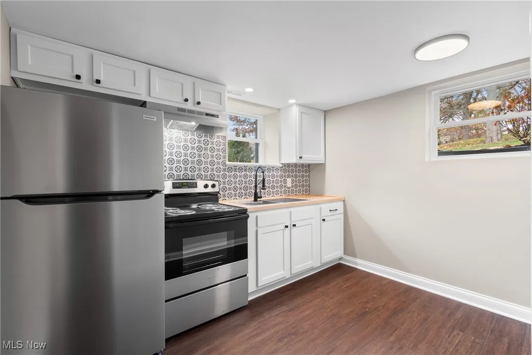 Kitchen with appliances with stainless steel finishes, decorative backsplash, dark wood-style floors, white cabinets, and light countertops