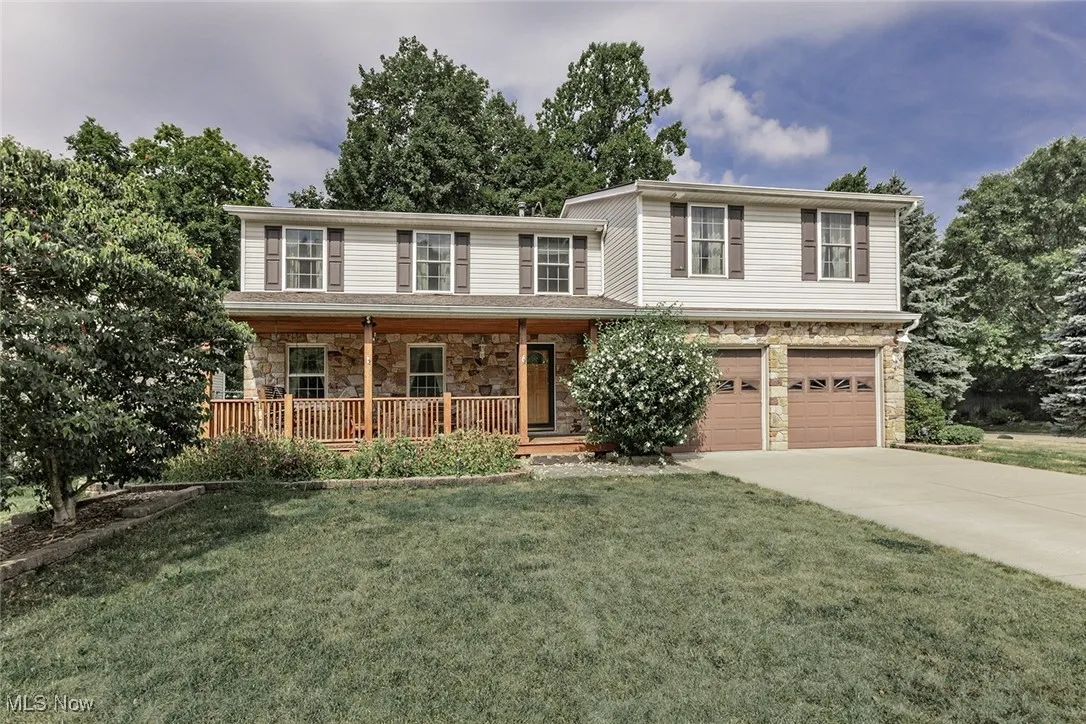 Traditional home with stone siding, driveway, a porch, an attached garage, and a front lawn
