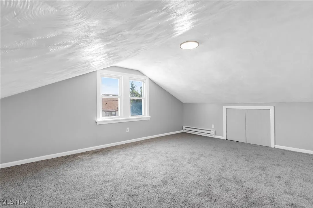 Bonus room with carpet flooring, lofted ceiling, a baseboard heating unit, and a textured ceiling