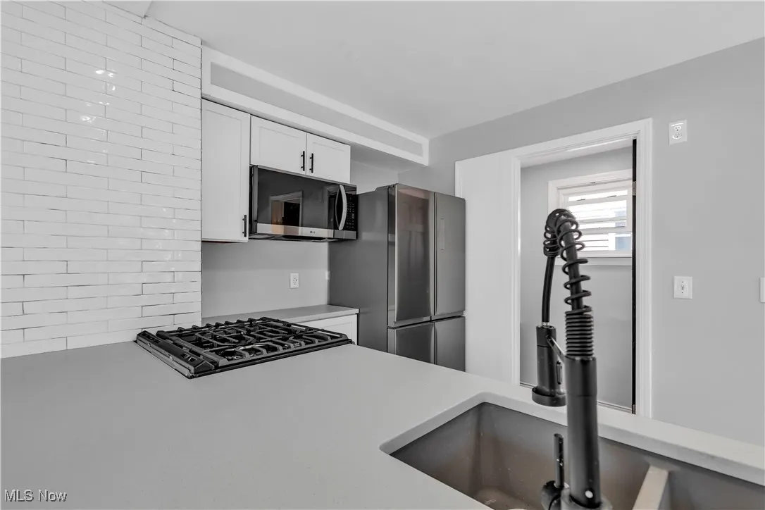 Kitchen with stainless steel microwave, white cabinetry, light countertops, and cooktop