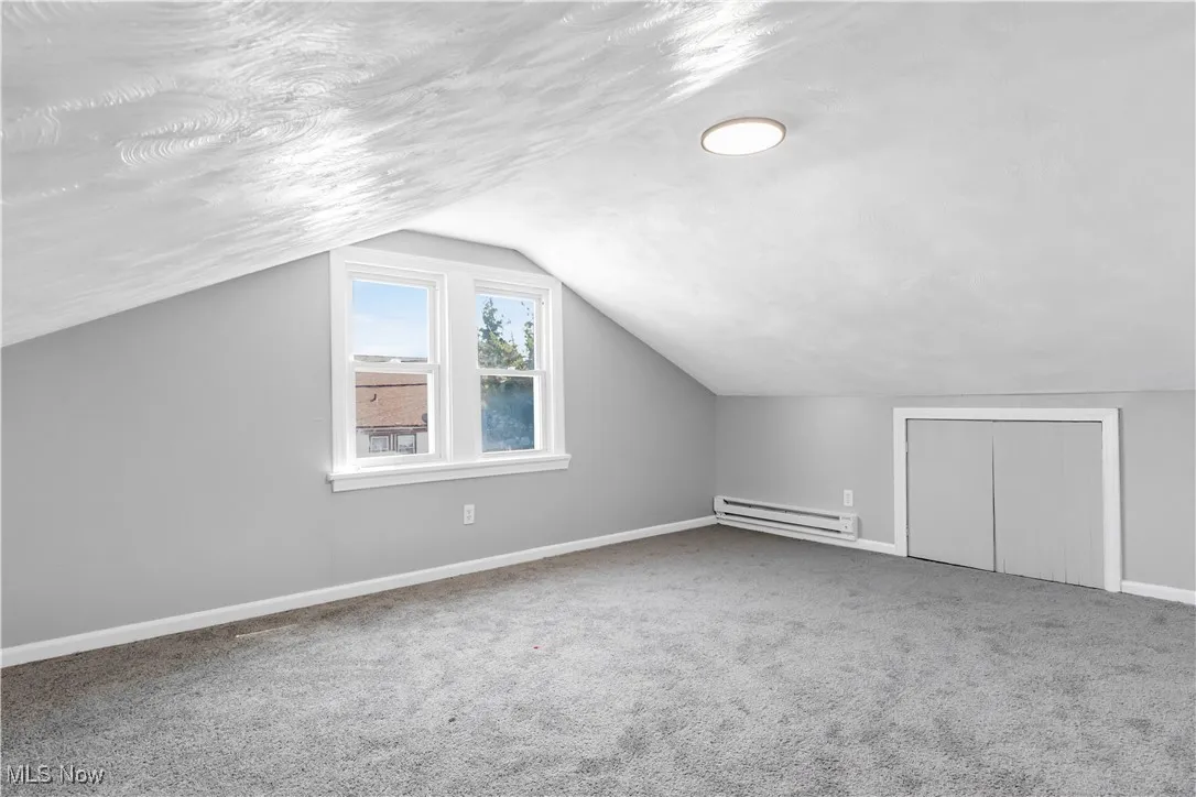 Bonus room with carpet floors, lofted ceiling, a baseboard heating unit, and a textured ceiling