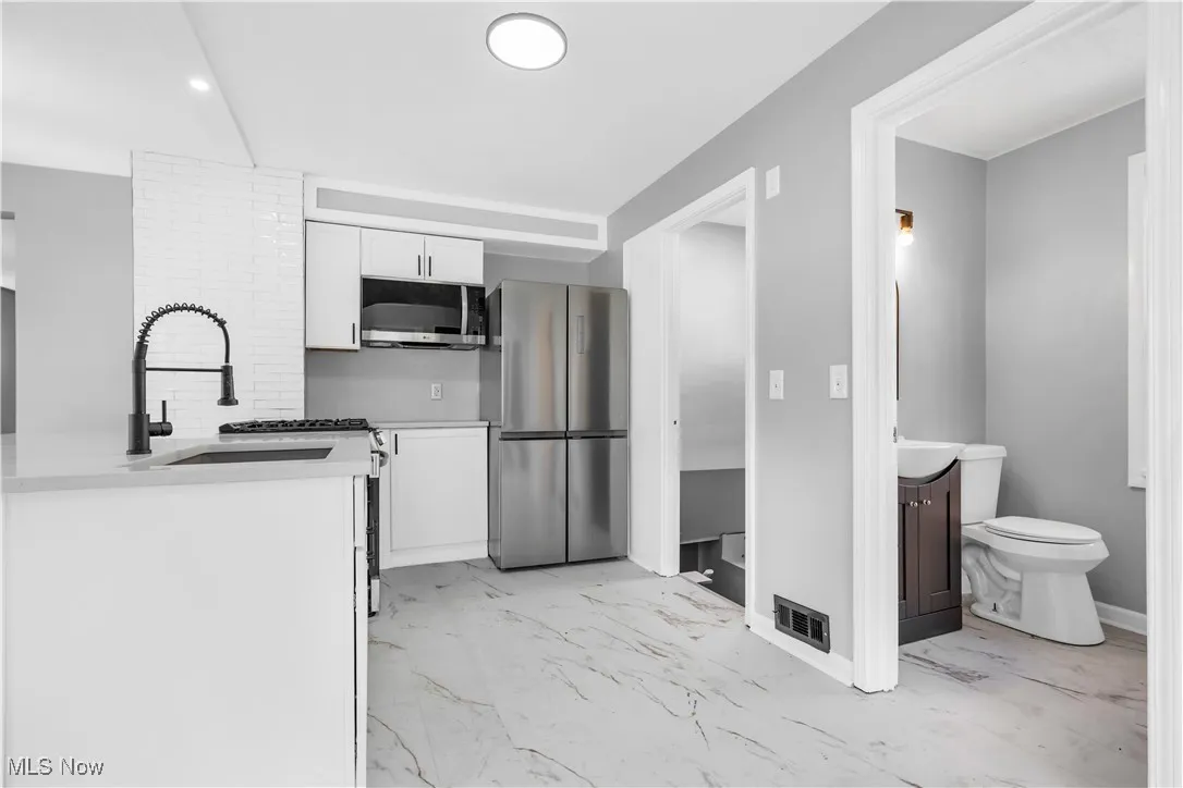 Kitchen featuring appliances with stainless steel finishes, white cabinets, light marble finish floors, and light countertops