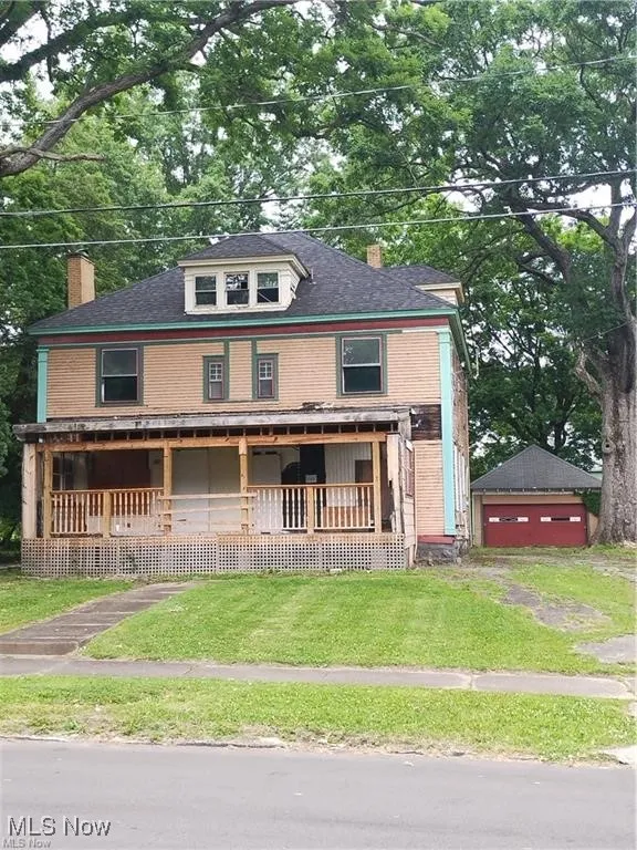 American foursquare style home with covered porch, a chimney, a front lawn, an outdoor structure, and a garage