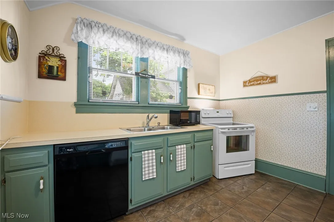 Kitchen with black appliances, wallpapered walls, light countertops, green cabinets, and a wainscoted wall