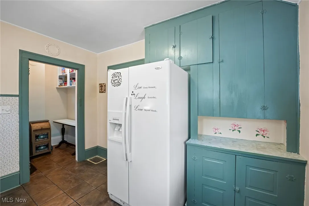 Kitchen with white fridge with ice dispenser, light countertops, dark tile patterned flooring, and blue​​‌​​​​‌​​‌‌​‌‌​​​‌‌​‌​‌​‌​​​‌​​ cabinetry