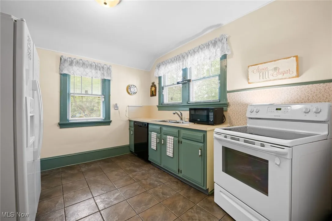 Kitchen with green cabinetry, black appliances, light countertops, and dark tile patterned flooring