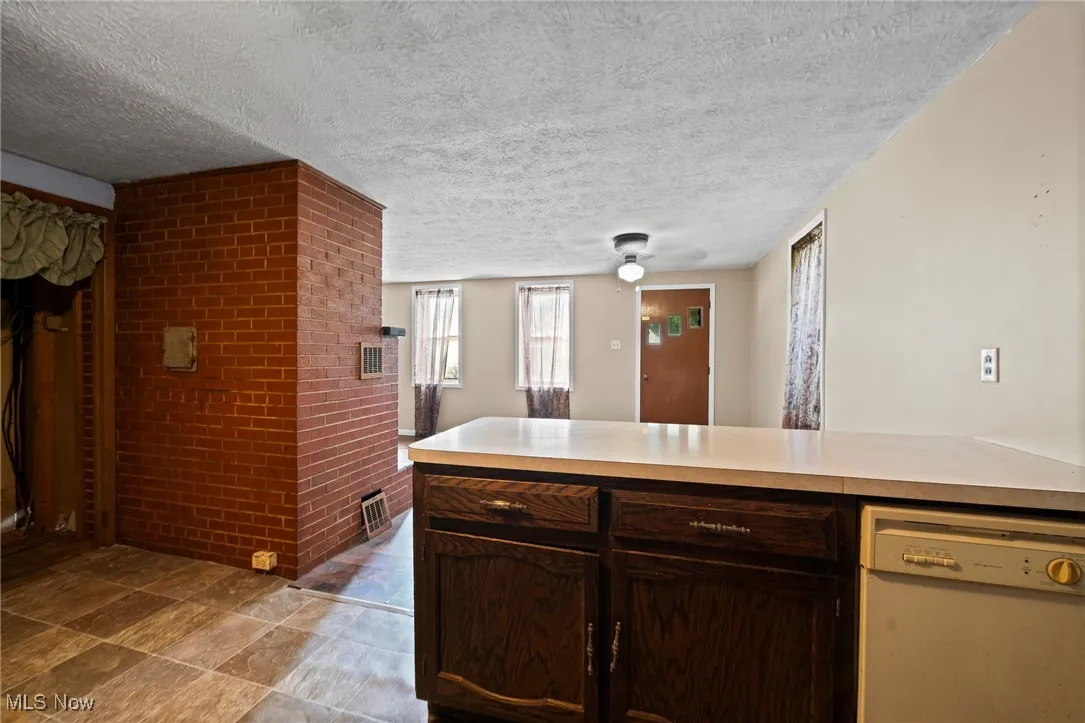 Kitchen with white dishwasher, a textured ceiling, brick wall, light countertops, and ceiling fan