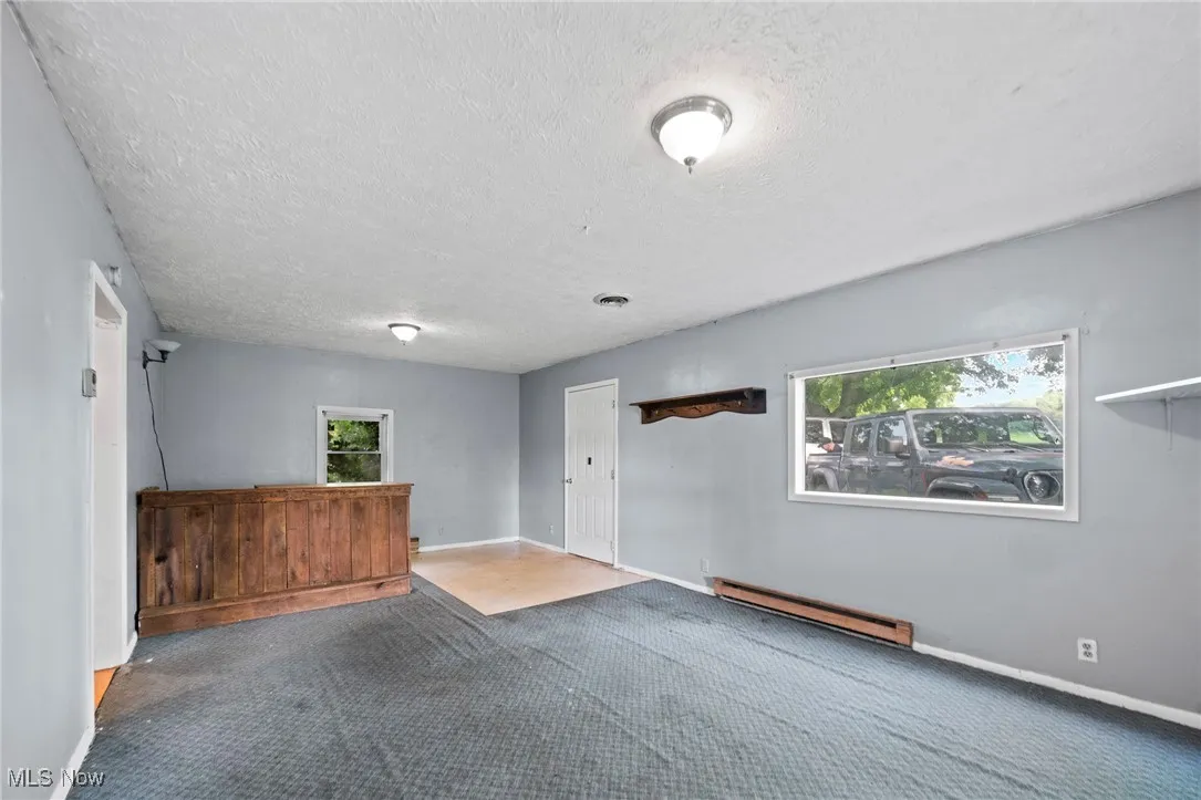 Spare room featuring a textured ceiling, a baseboard heating unit, and carpet floors