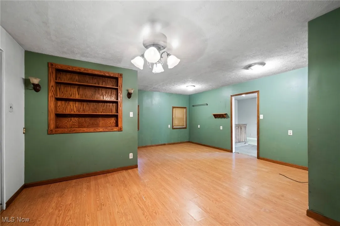 Spare room with a textured ceiling, built in shelves, wood finished floors, and ceiling fan