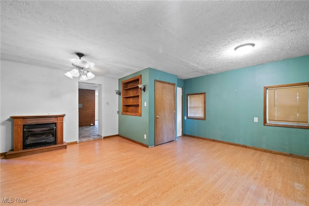 Unfurnished living room with a textured ceiling, light wood-type flooring, a ceiling fan, and a fireplace