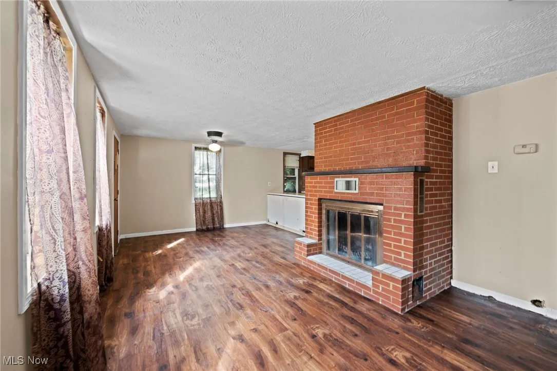 Unfurnished living room featuring wood finished floors, a textured ceiling, a brick fireplace, and ceiling fan