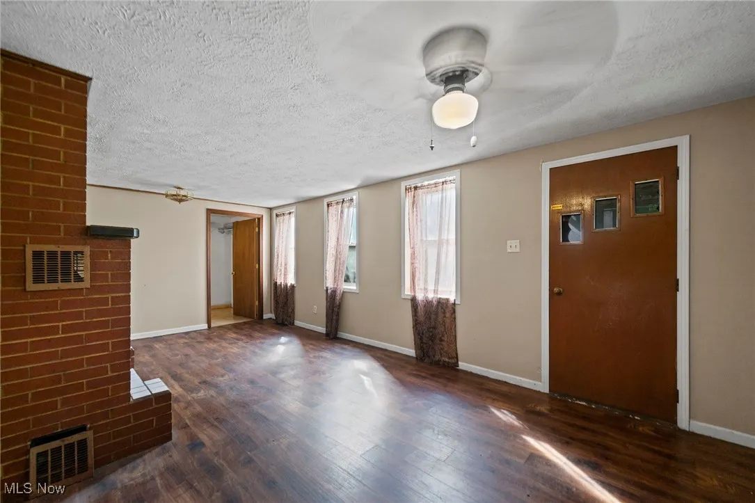 Unfurnished living room featuring a brick fireplace, a ceiling fan, wood finished floors, and a textured ceiling