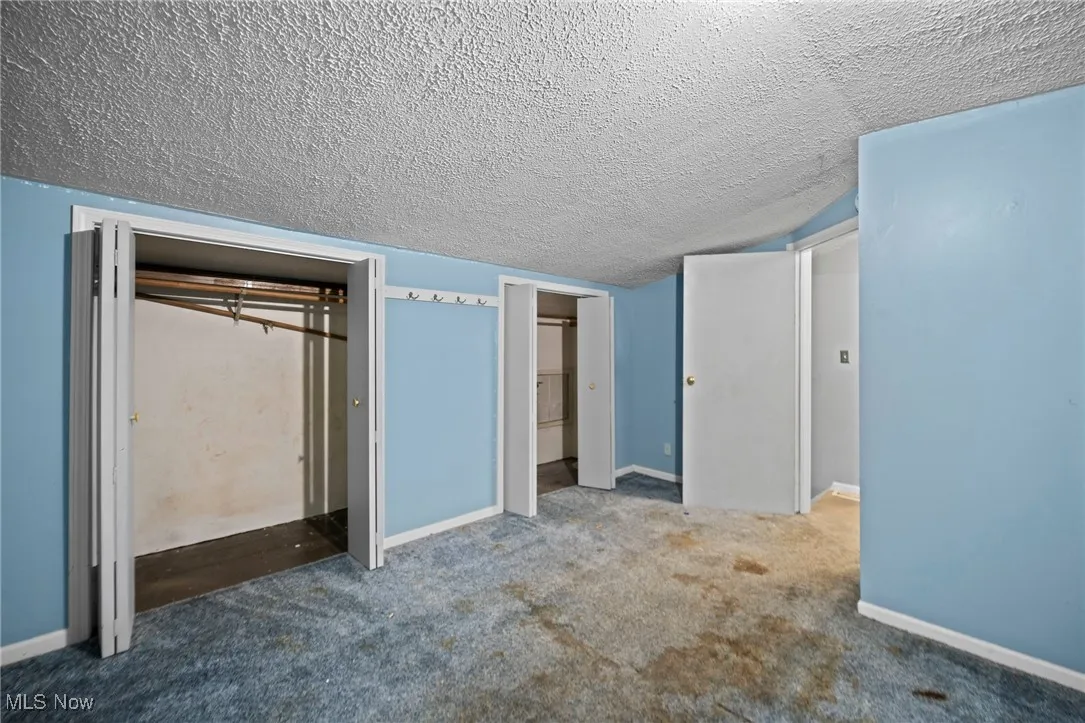 Unfurnished bedroom featuring a textured ceiling, carpet floors, and two closets