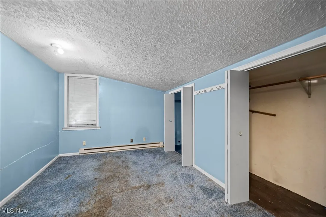 Unfurnished bedroom featuring a textured ceiling, carpet flooring, baseboard heating, and vaulted ceiling