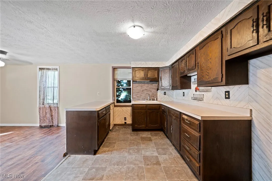 Kitchen with dark brown cabinetry, light countertops, backsplash, a textured ceiling, and ceiling fan