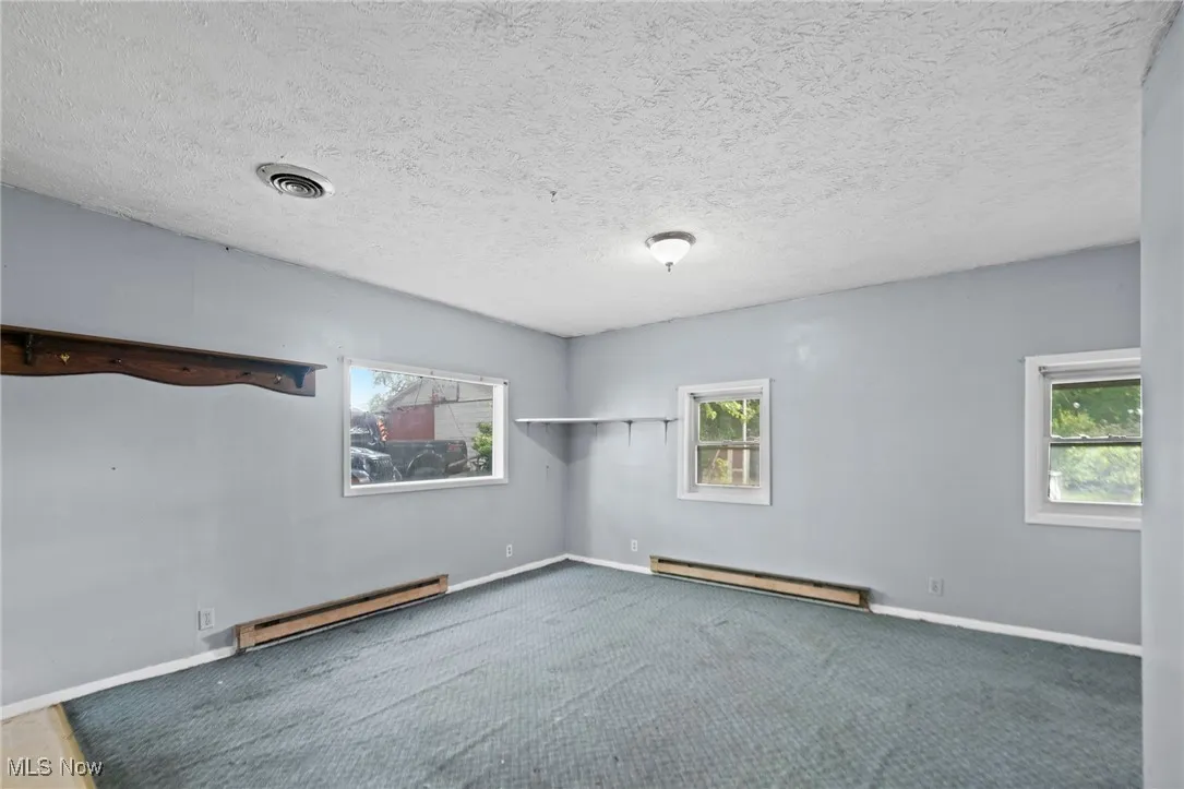 Carpeted spare room featuring a textured ceiling and a baseboard heating unit