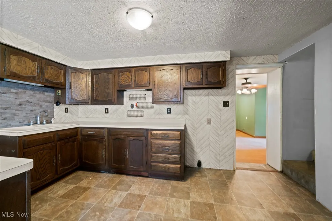 Kitchen featuring dark brown cabinets, light countertops, a textured ceiling, ceiling fan, and stone finish floors