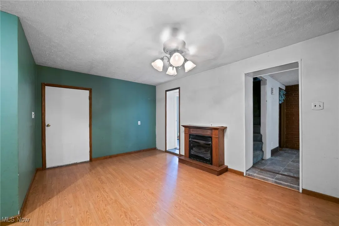 Unfurnished living room with a textured ceiling, a fireplace, wood finished floors, and ceiling fan