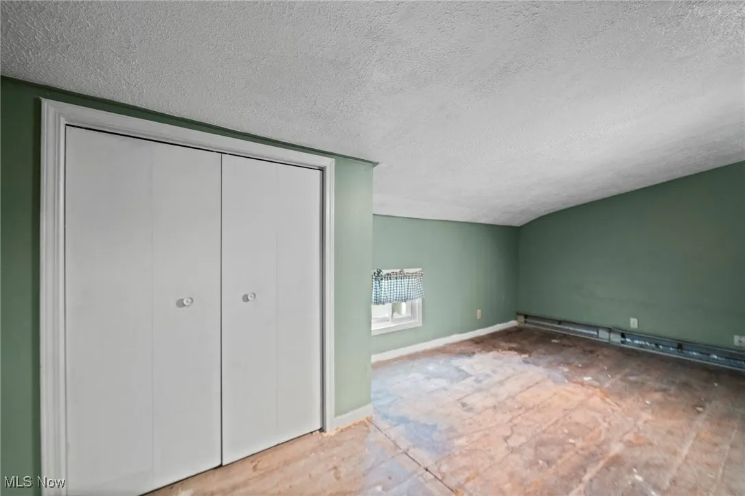 Unfurnished bedroom with a textured ceiling, baseboard heating, a closet, and vaulted ceiling