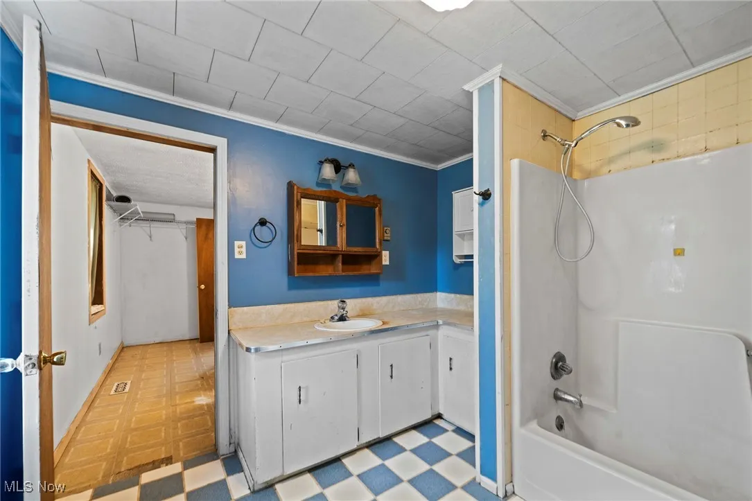 Bathroom with tile patterned floors, vanity, shower / bathtub combination, and ornamental molding