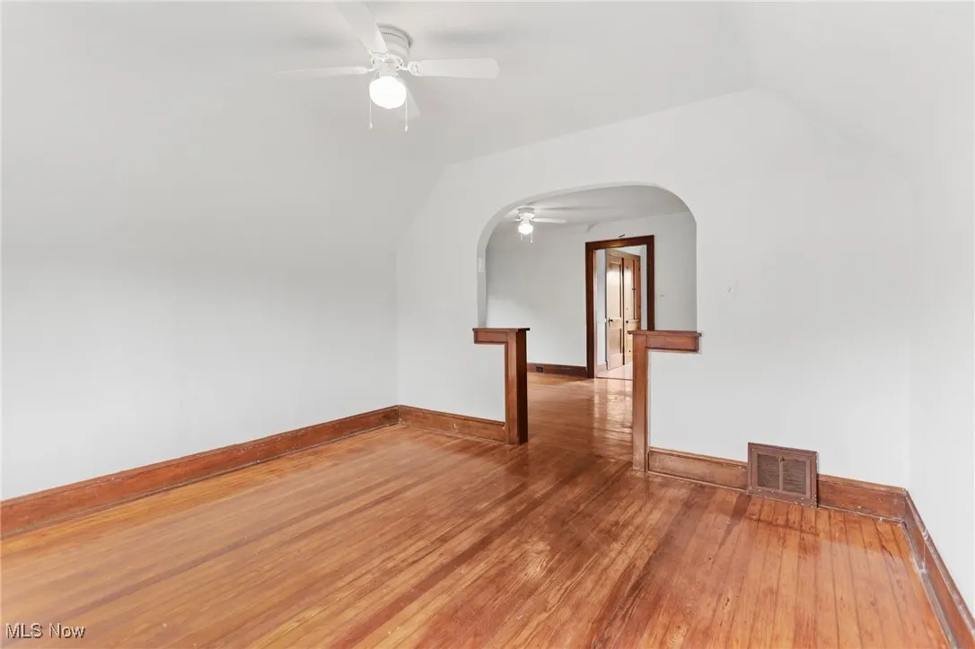 Spare room featuring arched walkways, a ceiling fan, light wood-type flooring, and lofted ceiling