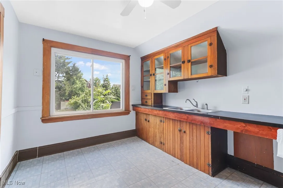 Kitchen with brown cabinets, ceiling fan, light floors, and glass insert cabinets