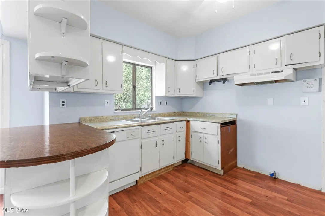 Kitchen with white dishwasher, dark wood-style flooring, open shelves, and white cabinets