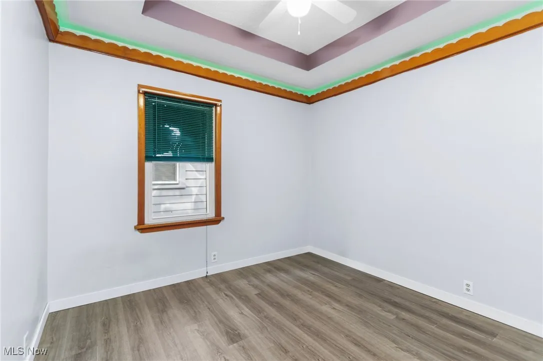 Empty room featuring a raised ceiling, wood finished floors, and a ceiling fan